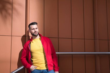Kırmızı ceketli yakışıklı bir genç, sarı tişörtlü ve merdivenin korkuluğuna yaslanmış kot pantolonlu. Güzellik kavramı, moda, modern, moda.