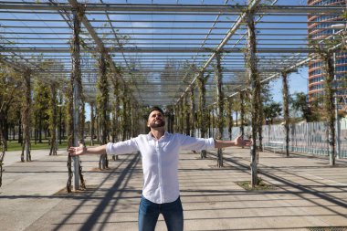 Sakallı, beyaz gömlek ve kot pantolon giyen, kolları açık, çok mutlu ve minnettar, gökyüzüne bakan yakışıklı bir genç. Mutluluğu kavra, başarıyı, minnettarlığı, Tanrı 'ya şükür..