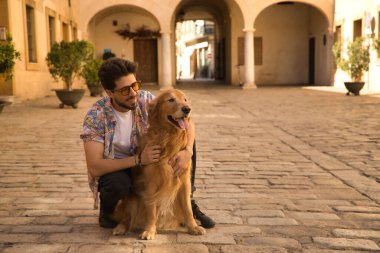 Young Hispanic man with beard and sunglasses hugging his dog very happy. Concept animals, dogs, love, pets, golden.