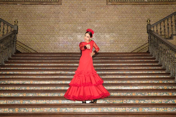Young teenage woman in red dance suit with ruffles and red carnations in her hair dancing flamenco on stairs. Flamenco concept, dance, art, typical Spanish dance.