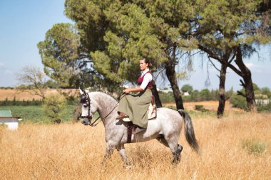 Woman horsewoman, young and beautiful, walking, riding her horse, in the countryside. Concept horse riding, animals, dressage, horsewoman, cowgirl.