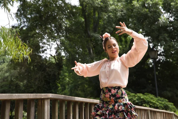 Young teenage woman in pink shirt, black skirt with flowers and pink carnations in her hair, dancing flamenco on wooden bridge. Flamenco concept, dance, art, typical Spanish dance.