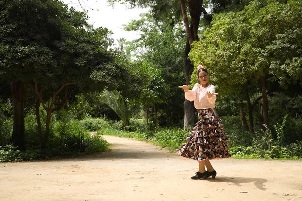 Young teenage woman in pink shirt, black skirt with flowers and pink carnations in her hair, dancing flamenco in an outdoor park. Flamenco concept, dance, art, typical Spanish dance.