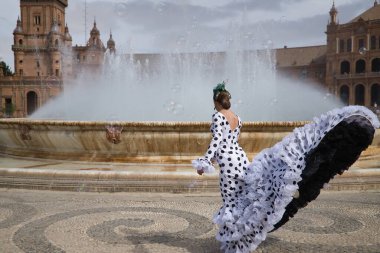 Young teenage woman in white suit with black polka dots, dancing flamenco in front of water fountain and surrounded by soap bubbles. Flamenco concept, dance, art, typical Spanish dance, bubbles.