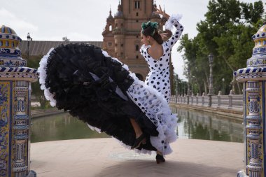 Siyah benekli, saçında yeşil karanfil olan, gölün kenarında flamenko dansı yapan beyaz dans kıyafetli genç bir kadın. Flamenko konsepti, dans, sanat, tipik İspanyol dansı.