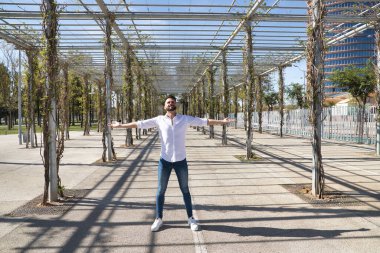 Sakallı, beyaz gömlek ve kot pantolon giyen, kolları açık, çok mutlu ve minnettar, gökyüzüne bakan yakışıklı bir genç. Mutluluğu kavra, başarıyı, minnettarlığı, Tanrı 'ya şükür..