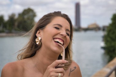 Genç, çekici, sarışın bir kadının portresi bir güneş gözlüğünün tapınağını ısırıyor, yüksek sesle gülüyor. Güzelliği, modayı, trendi, mutluluğu, kahkahayı, seyahati kavra.