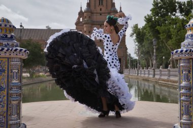 Siyah benekli, saçında yeşil karanfil olan, gölün kenarında flamenko dansı yapan beyaz dans kıyafetli genç bir kadın. Flamenko konsepti, dans, sanat, tipik İspanyol dansı.