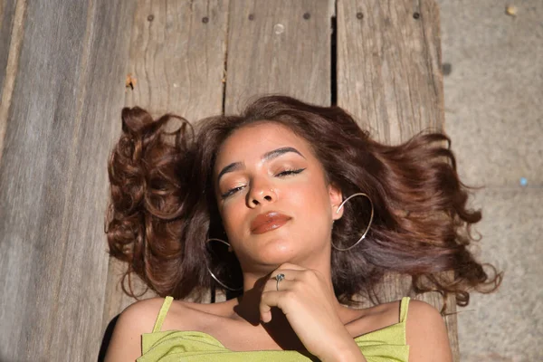 長い茶色の髪とシナモンの皮を持つ美しい若い女性の肖像画は 木製のベンチにカメラを見て横たわっ 美容コンセプト メイク ヘアスタイル ファッション トレンド — ストック写真