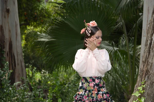 Young teenage woman in pink shirt, black skirt with flowers and pink carnations in her hair, dancing flamenco surrounded by greenery. Flamenco concept, dance, art, typical Spanish dance.