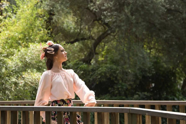 Young teenage woman in pink shirt, black skirt with flowers and pink carnations in her hair, dancing flamenco on wooden bridge. Flamenco concept, dance, art, typical Spanish dance.