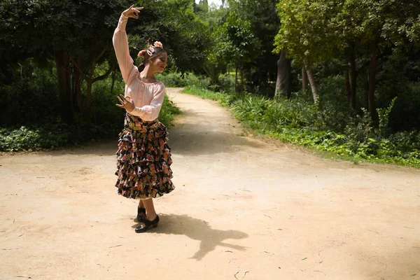 Young teenage woman in pink shirt, black skirt with flowers and pink carnations in her hair, dancing flamenco in an outdoor park. Flamenco concept, dance, art, typical Spanish dance.