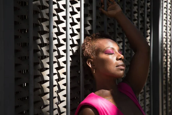 穿着粉色T恤和粉色眼罩的非洲裔美国女人的画像 眼睛闭着 紧紧抓住在阳光下的栅栏 概念放松 — 图库照片