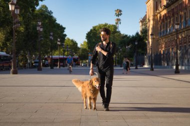 Sakallı, güneş gözlüklü, siyah gömlekli ve sırt çantalı genç bir İspanyol köpeğiyle şehirde dolaşıyor. Hayvanlar, köpekler, aşk, evcil hayvanlar, altın.
