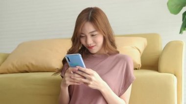 Güzel bir Asyalı kadın oturma odasında dinleniyor. Elinde akıllı bir telefonla arkadaşlarıyla sohbet ederken kendini mutlu hissediyordu. Çevrimiçi iletişim teknolojisi kavramı, yeni yaşam tarzı