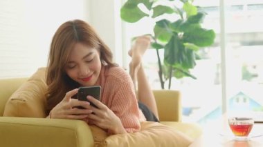 Güzel Asyalı kadın evde mutlu bir şekilde gülümsüyor telefonda yalan söylüyor, çevrimiçi video görüşmeleri yapıyor, arkadaşlarıyla sohbet ediyor. Modern iletişim teknolojisi kavramı, sosyal uzaklık.