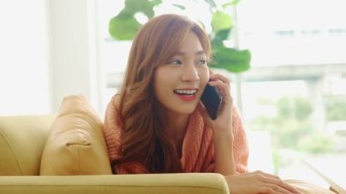 Güzel Asyalı kadın evde mutlu bir şekilde gülümsüyor telefonda yalan söylüyor, çevrimiçi video görüşmeleri yapıyor, arkadaşlarıyla sohbet ediyor. Modern iletişim teknolojisi kavramı, sosyal uzaklık.