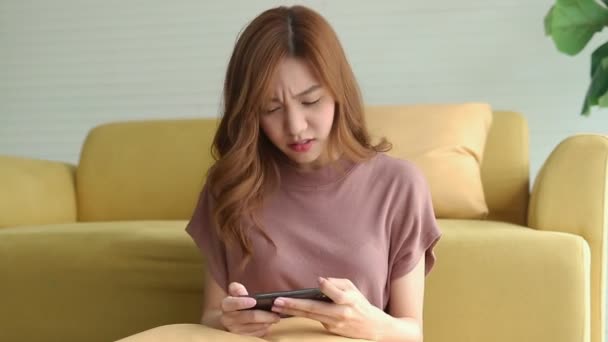 美丽的亚洲女人在一个公寓里放松 她在智能手机上玩网络游戏很开心 使用现代通信技术的概念 — 图库视频影像