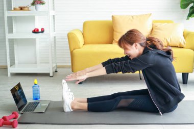 Güzel Asyalı kadın egzersizini apartman dairesinde yaptı. Antrenörü takip eden egzersizleri dizüstü bilgisayarındaki çevrimiçi videolar vasıtasıyla yaptı. Sağlık hizmeti kavramı, yeni normal