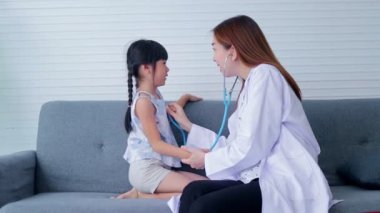 Asyalı güzel kadın doktor nabzını ölçmek için steteskop tutuyor. Küçük tatlı bir kızın kalp ritmini kontrol ediyor. İkisi de kanepede oturuyordu. Hastanelerdeki sağlık hizmetleri kavramı, çocuk sağlığı kontrolleri.