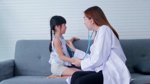 可愛い女の子の脈 心臓のリズムをチェックするために聴診器を持っているアジアの美しい女性医師彼らは両方ともソファの上に座っていました 病院での医療サービスの概念 子供の健康診断 — ストック動画