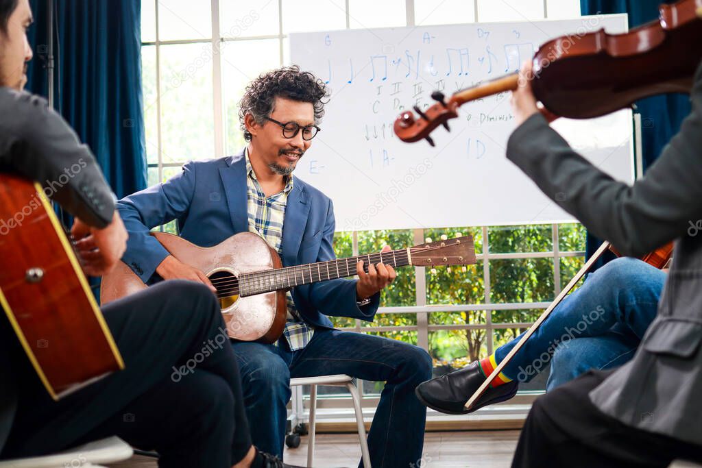 A group of Asian musicians playing guitar and violin sitting on classical music. They are fun and happy. Concept of learning classical music. Live music and bands