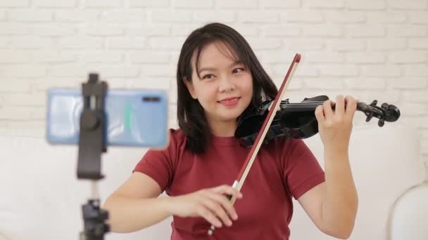 アジアの女性教師は スマートフォンのオンラインビデオを介して自宅からクラシック楽器のバイオリンを再生する方法を学生を教えています クラシック音楽教育の概念は 自宅からオンラインで勉強 新しい普通の生活 — ストック動画