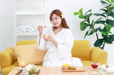 Evde spa yapan güzel bir Asyalı kadın cildine sürmek için elinde bir fincan doğal bal tutuyor. Güzellik konsepti iyi sağlık için vücudu rahat, rahat ve güzel yapar..