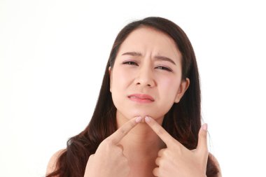Asyalı uzun saçlı güzel bir kadının yüzünde sivilce var. Çenesindeki sivilceyi sıkmak için elini kullandı. Acıyı hissediyordu. Güzellik konsepti. Güzel olmak için yüzüne bakmak. akne tedavisi