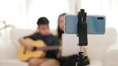 Asyalı anne ve oğlu evde oturma odasında birlikte müzik çalıyorlar. Live Mobile 'da akıllı telefonlardan yayın yapıyorlar. Aile kavramı, çevrimiçi müzik çalmak. Modern iletişim.