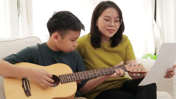 Asian Mother Son Sitting White Sofa House Son Plays Guitar — 图库视频影像