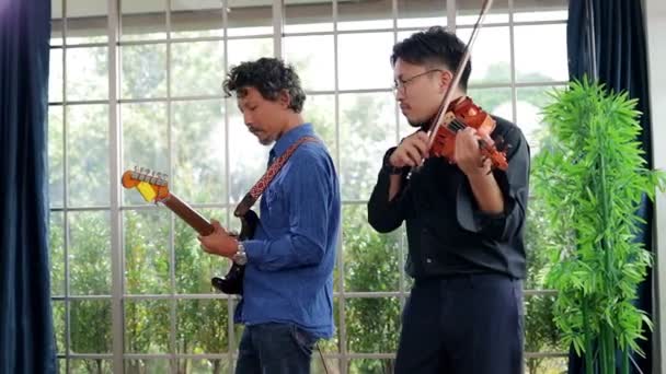 2人のアジア人男性がクラシック楽器のバイオリンとギターを練習室で一緒に演奏します どちらも音楽を演奏するのが好きだ ライブ音楽やバンド演奏の概念 — ストック動画