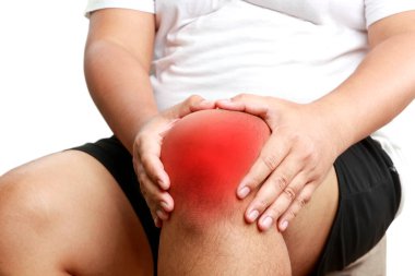 Beyaz gömlek giyen şişman bir adam ellerini dizlerinin üstüne koydu. Spor yaparken dizinden yaralanmış. Obezite konsepti. Kemik iltihabı da dahil olmak üzere çeşitli hastalıkların aşırı kilolu riski.
