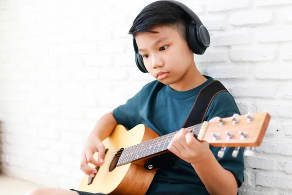 身穿黑色音乐耳机的亚洲男孩坐在屋里弹吉他 音乐学习的概念 音乐熟练程度的训练 复制空间 — 图库照片