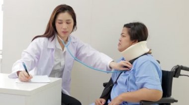 Asyalı kadın doktor muayene odasında tekerlekli sandalyede oturan obez hastaların kalp ritmini dinlemek için steteskop kullanıyor. Hastanede tıbbi hizmet kavramı