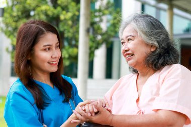 Cerrahi elbiseler giyen doktorlar, el ele tutuşanlar, tekerlekli sandalyelerde oturan yaşlı hastalar, tedavi için endişelenmiyorlar. Hastanede tıbbi hizmet kavramı