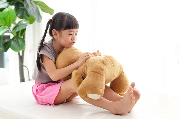 可爱的亚洲小女孩 玩得很开心她把一只棕色的大泰迪熊抱在白色的床上 友谊的概念 — 图库照片