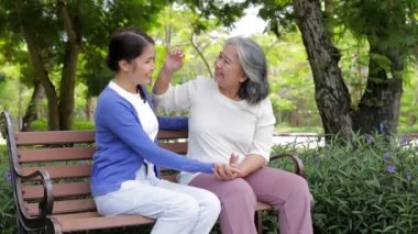 Kızı ve yaşlı annesi sabah parkta otururken mutlu bir şekilde gülümsüyorlar. Aile kavramı. Emeklilik yaşındakilerin sağlık hizmetleri. Yaşlılara bakıcılık.