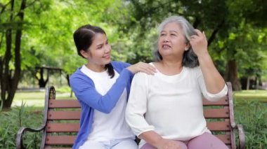 Kızı ve yaşlı annesi sabah parkta otururken mutlu bir şekilde gülümsüyorlar. Aile kavramı. Emeklilik yaşındakilerin sağlık hizmetleri. Yaşlılara bakıcılık.