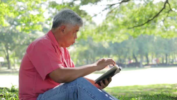 Ασιάτης Ηλικιωμένος Που Κάθεται Στο Πάρκο Διαβάζοντας Ένα Βιβλίο Πρωί — Αρχείο Βίντεο