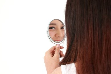 Güzel Asyalı kadın aynayı tutuyor ve yüzüne bakıyor. O mutlu bir şekilde gülümsedi. Güzellik konsepti, güzellik, cilt bakımı. Beyaz arka plan. Boşluğu kopyala