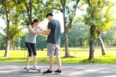 Asyalı çift sabah birlikte egzersiz yapıyor. Parkın sokaklarında temel kaykay antrenmanı yapıyorlar. Sağlık için spor yapmak seni güçlü ve mutlu yapar..