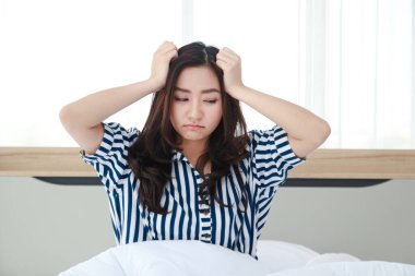 Yatakta oturan Asyalı kadın baş ağrısı. Kendini stresli hissetti ve uyuyamadı. Sağlık hizmeti konsepti. Yeterli dinlenme yok. Migrenim tuttu. Uyandıktan sonra başım ağrıyor..