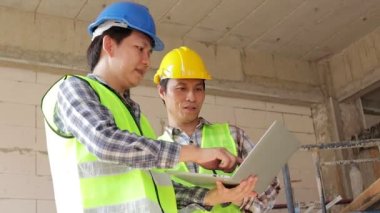 Engineers and construction contractors Holding a laptop to discuss building construction plans at the outdoor site. Real estate project concepts, building construction cooperation.