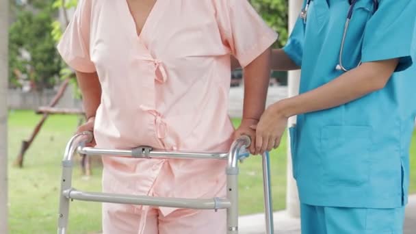 外科用ガウンを着た女性医師が高齢者の世話をする 体を強くするために物理的な療法を行うために歩くをサポートします 病院での医療サービスの概念は — ストック動画