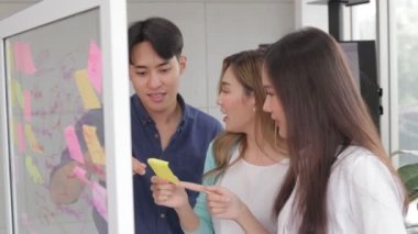 A group of young startup entrepreneurs Meeting to plan business direction for quick success Stick the note paper on the glass board. Entrepreneurial concept. modern business