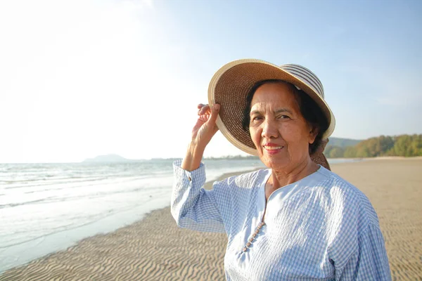 Smiling Asian elderly woman enjoying traveling Standing on the beach in the evening. The concept of tourism for the elderly. Retirement living and health care. copy space
