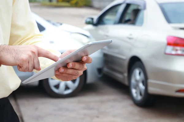 Auto insurance concept. A man, a company officer holding a tablet, takes pictures and records the accident car to inform the insurance company.