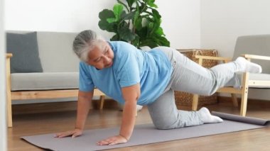 Asian elderly woman exercising at home Do a kneeling pose with your legs extended behind you. Social distancing. Health care of the elderly. sports concept