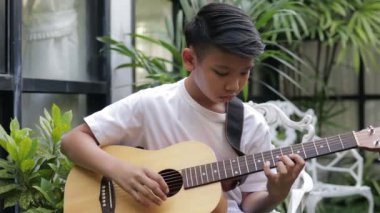 Asian boys practice playing acoustic guitar in the garden at home. Music learning concept, learning and practice.
